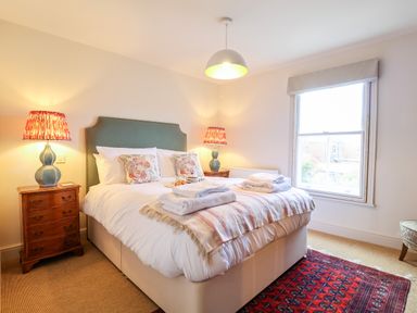 A bedroom with a bed with white bedding two bedside tables with lamps and a window at Collett House in Southwold