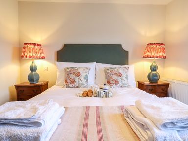 A bedroom with a bed featuring patterned cushions and a tray with croissants and tea cups at Collett House in Southwold