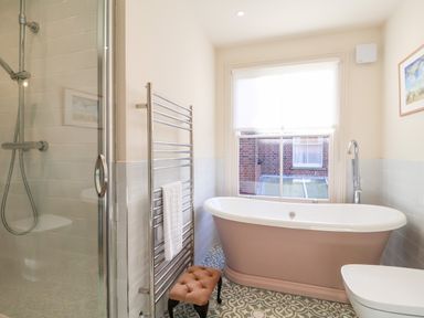 A bathroom with a freestanding bathtub next to a window a glass shower enclosure a towel rack and a small cushioned stool at Collett House in Southwold