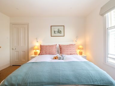 A bedroom with a double bed with patterned pillows two bedside tables with lamps a door and a window at Collett House in Southwold