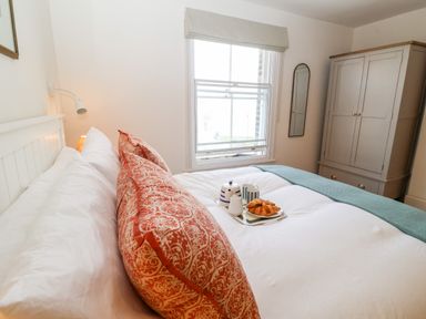 A bedroom with a bed featuring white sheets and patterned pillows next to a window and a wardrobe at Collett House in Southwold