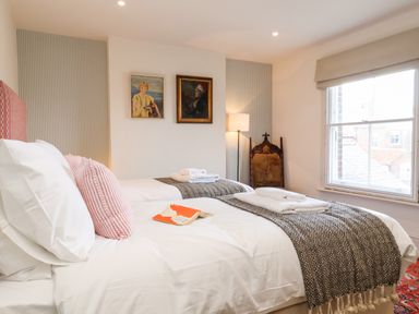 A bedroom with two single beds a window and framed paintings on the wall at Collett House in Southwold