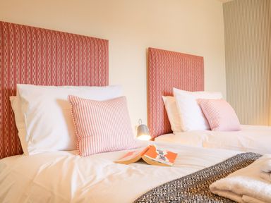 A bedroom with two single beds with red patterned headboards and striped pillows at Collett House Southwold