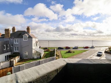 A view from a balcony overlooking a street with parked cars a lawn a gray house and the sea at Collett House in Southwold