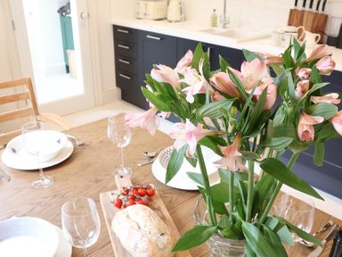 A kitchen with a wooden table set with plates wine glasses flowers bread and tomatoes at Collett House Southwold