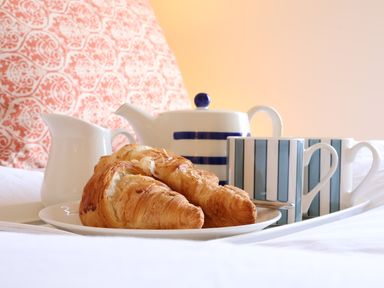 A tray with croissants teapot milk jug and striped mugs on a bed with patterned pillow at Collett House Southwold