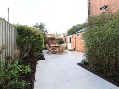 An outdoor patio area with a wooden table and chairs surrounded by plants and a brick building at Collett House in Southwold