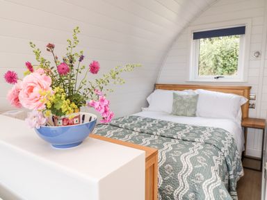 A bedroom with a bed covered in a green patterned quilt and a flower arrangement on a white surface at Ash in Saltash