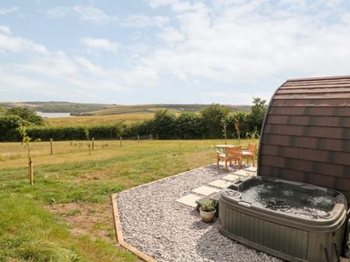 An outdoor area with a hot tub a table with two chairs and grassy fields in the background at Ash in Saltash