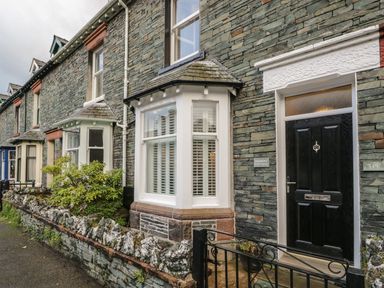 Stone exterior of a house with black front door and white bay window at Derwent Cottage in Keswick
