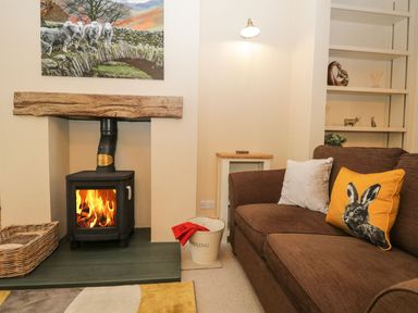 A living room with a fireplace and wood burner next to a brown sofa with animal print cushions at Derwent Cottage in Keswick