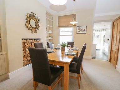 A dining room with a wooden table set for six with black chairs and a stack of firewood in the fireplace at Derwent Cottage in Keswick