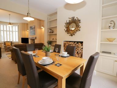 A dining area with a wooden table set for six and a living room with sofas and a TV at Derwent Cottage in Keswick