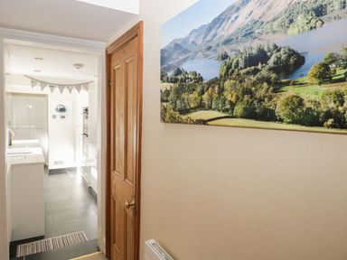 A hallway with a wooden door and a large landscape picture on the wall leading to a modern kitchen at Derwent Cottage in Keswick