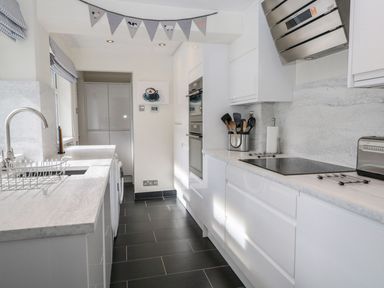 A kitchen with white cabinets black floor tiles and cooking utensils at Derwent Cottage in Keswick