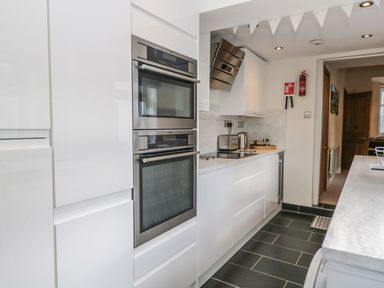 A modern kitchen with white cabinets built in oven stovetop and countertop appliances at Derwent Cottage Keswick