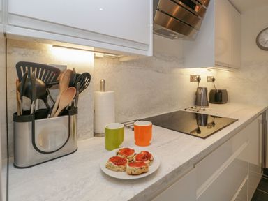 A kitchen counter with cooking utensils in a holder a roll of paper towels a plate with scones and jam two mugs a stove kettle and toaster at Derwent Cottage Keswick