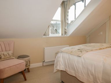 A bedroom with a bed blanket a pink chair an ottoman and a window at Derwent Cottage in Keswick