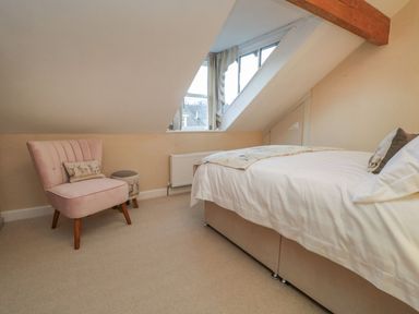 A bedroom with a sloped ceiling bed pink chair and a window at Derwent Cottage Keswick