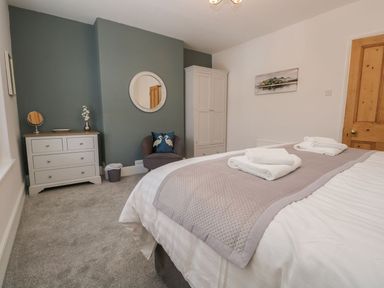 A bedroom with a bed with towels on it a chair a wardrobe and a chest of drawers at Derwent Cottage Keswick