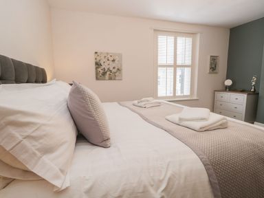 A bedroom with a bed made with pillows and towels by the window and a dresser with a mirror and vase at Derwent Cottage in Keswick