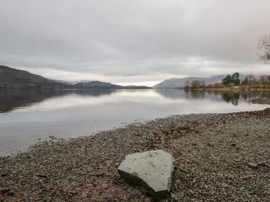 A lake with mountains in the background and a rocky shore in the foreground at Derwent Cottage in Keswick