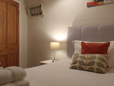 A bedroom with a bed white bedding decorative pillows a bedside table lamp wooden door and wall-mounted hooks at Derwent Cottage in Keswick