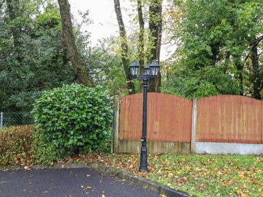 A black street lamp next to a wooden fence with dense green trees and bushes behind it at Hazelwood in Leap County Cork
