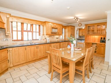 A kitchen with wooden cabinets a wooden dining table with six chairs and a tiled floor at Hazelwood in Leap County Cork