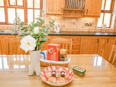 A kitchen with wooden cabinets a vase with white flowers a basket with tea coffee and sugar on a table with plate of pastries and butter at Hazelwood in Leap County Cork