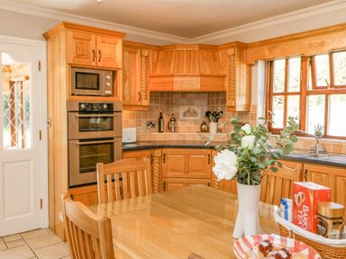 A kitchen with wooden cabinets a dining table with chairs a vase with flowers and a window at Hazelwood in Leap County Cork