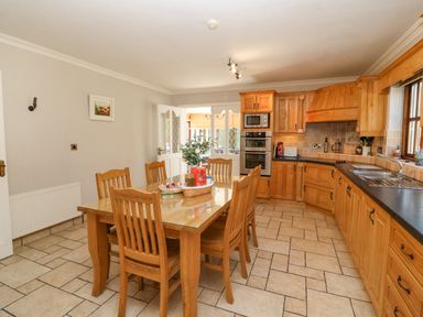 A kitchen with wooden cabinets a dining table with six chairs and tiled floor at Hazelwood in Leap County Cork