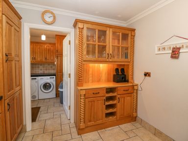 A kitchen area with wooden cabinets and a washing machine visible through an open door at Hazelwood in Leap County Cork