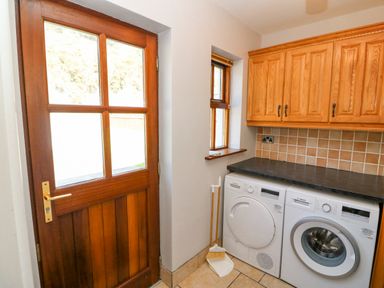 A laundry room with a wooden door a window washing machine dryer and wooden cabinets at Hazelwood in Leap County Cork