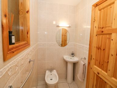 A small bathroom with a bidet pedestal sink round mirror light wooden door and window frame at Hazelwood in Leap County Cork