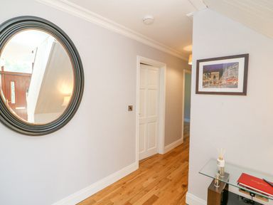 A hallway with wooden flooring a round mirror on the wall a framed picture and a glass table with books and a reed diffuser at Hazelwood in Leap County Cork