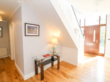 An entryway with wooden floor a glass table with a lamp and a red book under stairs a wooden front door with glass panels at Hazelwood in Leap County Cork