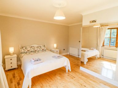 A bedroom with a bed two bedside tables two lamps wooden floor and a mirrored wardrobe at Hazelwood in Leap County Cork