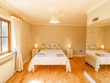 A bedroom with a bed two bedside tables with lamps a window with curtains and a mirrored wardrobe at Hazelwood in Leap County Cork
