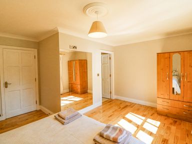 A bedroom with wooden floor a bed a wardrobe and a mirrored wall at Hazelwood in Leap County Cork