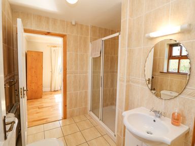 A bathroom with a shower cubicle a round mirror a sink and a view into a room with wooden flooring and a wardrobe at Hazelwood in Leap County Cork