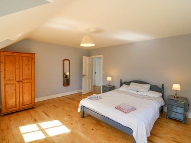 A bedroom with a double bed bedside tables with lamps a wooden wardrobe and a wall mirror at Hazelwood in Leap County Cork