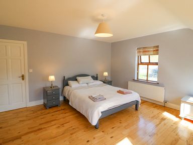A bedroom with a double bed between two bedside tables with lamps a window with a blind and wooden floor at Hazelwood in Leap County Cork