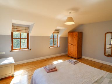 A bedroom with two windows a wooden wardrobe a wall mirror and a bed with folded towels at Hazelwood in Leap County Cork