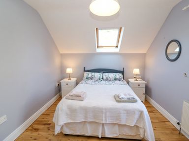A bedroom with a double bed two bedside tables with lamps a skylight window and a round mirror on the wall at Hazelwood in Leap County Cork