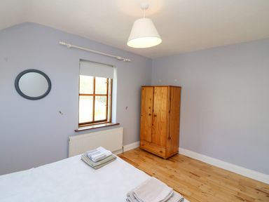 A bedroom with a wooden wardrobe a bed with folded towels a window and a round mirror on the wall at Hazelwood in Leap County Cork