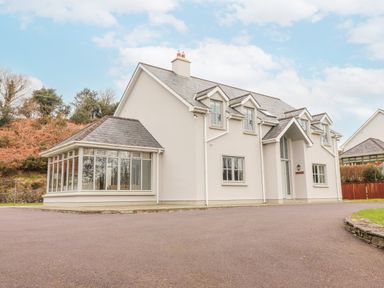 A detached two-story house with multiple windows and a glass extension on a paved driveway at Hazelwood in Leap County Cork