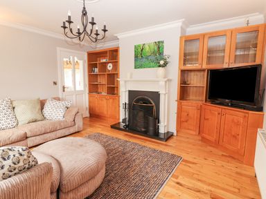 A living room with a fireplace two wooden bookshelves a television beige sofa and an ottoman at Hazelwood in Leap County Cork