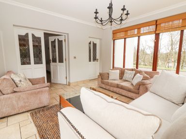 A living room with beige and brown sofas a glass coffee table a rug tiled floor white doors and large windows with wooden blinds at Hazelwood in Leap County Cork