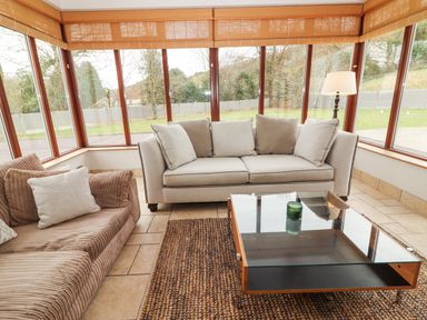 A sunroom with large windows a beige sofa a brown corduroy sofa a glass coffee table and a floor lamp at Hazelwood in Leap County Cork
